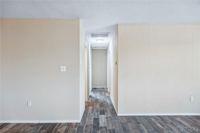 hall featuring a textured ceiling, dark wood-type flooring, attic access, and baseboards