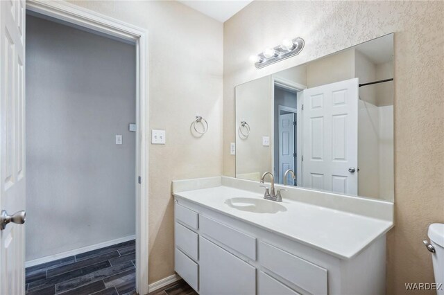 full bathroom with toilet, wood tiled floor, vanity, baseboards, and walk in shower