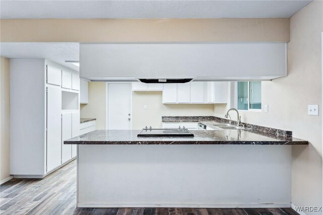 kitchen featuring black electric cooktop, a peninsula, wood finished floors, a sink, and white cabinetry