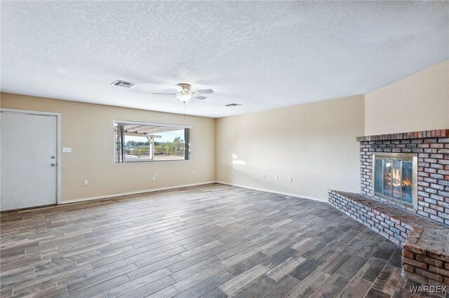 unfurnished living room featuring a fireplace, visible vents, ceiling fan, a textured ceiling, and wood finished floors