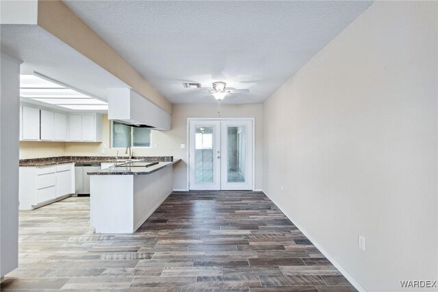 kitchen with a peninsula, white cabinets, french doors, stainless steel dishwasher, and dark countertops