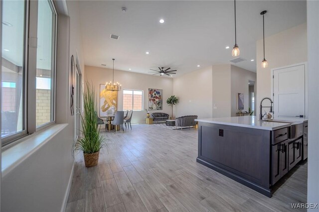 kitchen featuring pendant lighting, a center island with sink, light countertops, visible vents, and open floor plan