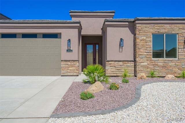 view of front of property featuring a garage, concrete driveway, stone siding, a tiled roof, and stucco siding