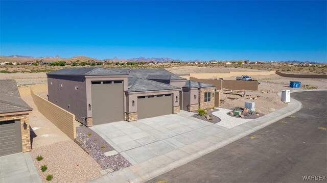 prairie-style home featuring an attached garage, a mountain view, concrete driveway, stone siding, and stucco siding