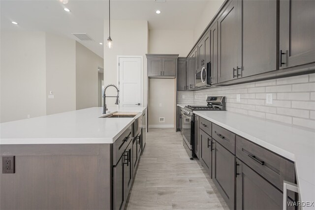 kitchen featuring tasteful backsplash, appliances with stainless steel finishes, light countertops, pendant lighting, and a sink