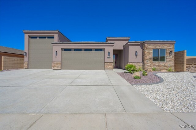 prairie-style house with stone siding, concrete driveway, an attached garage, and stucco siding