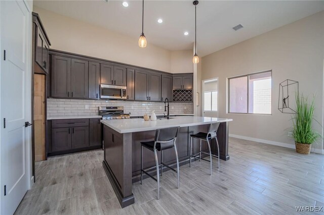 kitchen with range, stainless steel microwave, hanging light fixtures, a kitchen island with sink, and light countertops