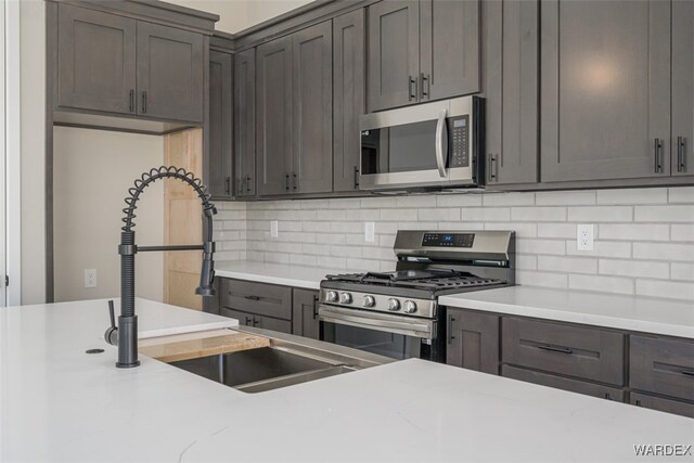 kitchen with appliances with stainless steel finishes, light countertops, a sink, and decorative backsplash