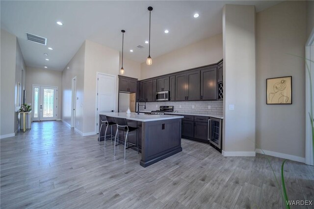 kitchen featuring light countertops, appliances with stainless steel finishes, decorative backsplash, an island with sink, and decorative light fixtures