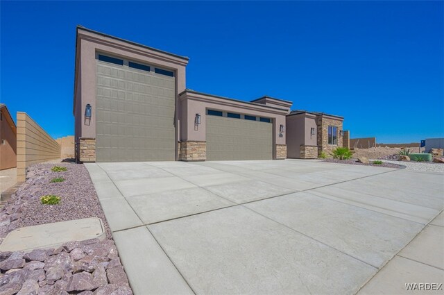 prairie-style house featuring stucco siding, an attached garage, fence, stone siding, and driveway