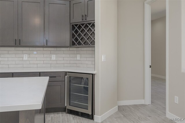 bar featuring wine cooler, a dry bar, light wood finished floors, decorative backsplash, and baseboards