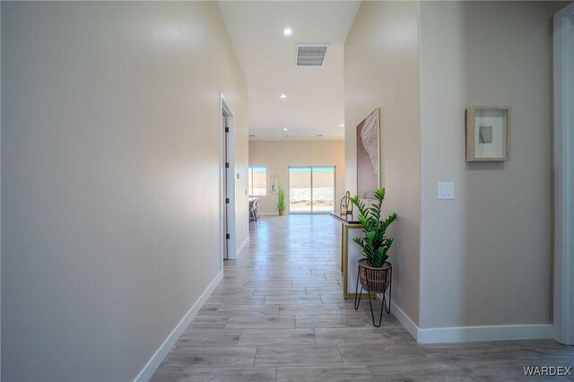 hall featuring light wood finished floors, baseboards, and visible vents