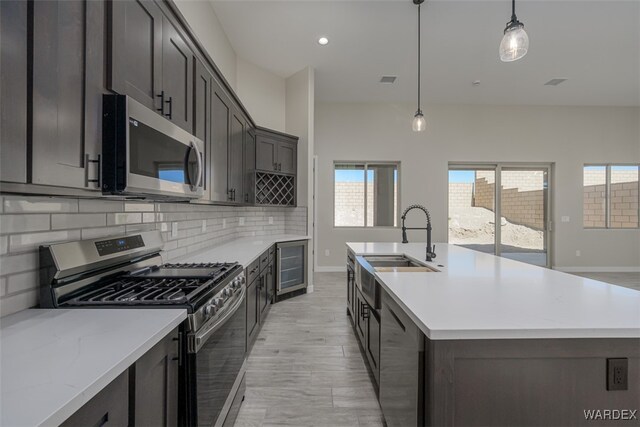 kitchen featuring tasteful backsplash, an island with sink, hanging light fixtures, light stone countertops, and stainless steel appliances