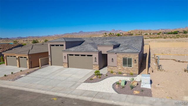 prairie-style house with an attached garage, a mountain view, stone siding, concrete driveway, and stucco siding