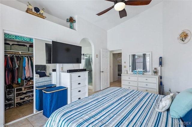 bedroom with light tile patterned floors, arched walkways, a ceiling fan, high vaulted ceiling, and a closet