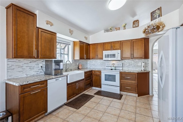 kitchen featuring vaulted ceiling, white appliances, a sink, and brown cabinets