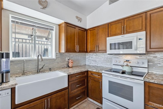 kitchen with light tile patterned floors, backsplash, brown cabinetry, a sink, and white appliances