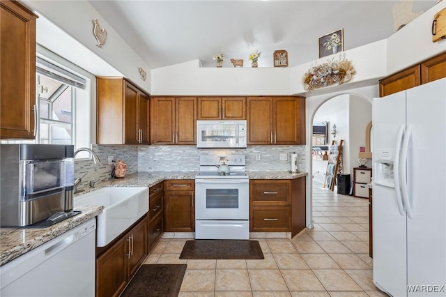 kitchen with arched walkways, white appliances, a sink, vaulted ceiling, and tasteful backsplash