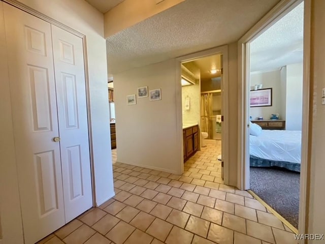 hall featuring a textured ceiling, baseboards, and light tile patterned floors