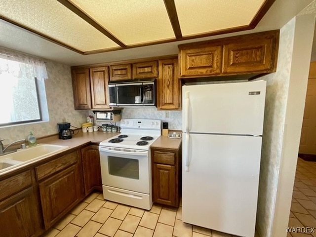 kitchen with white appliances, a sink, light countertops, brown cabinetry, and wallpapered walls