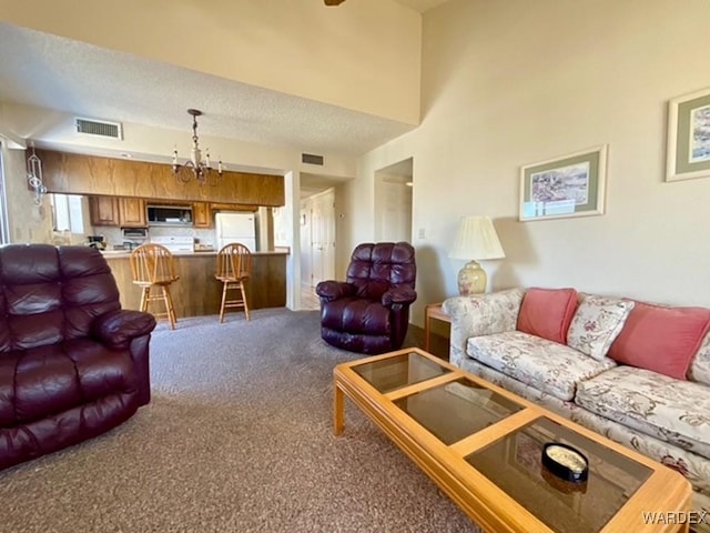 living area featuring visible vents, a notable chandelier, a textured ceiling, and carpet flooring