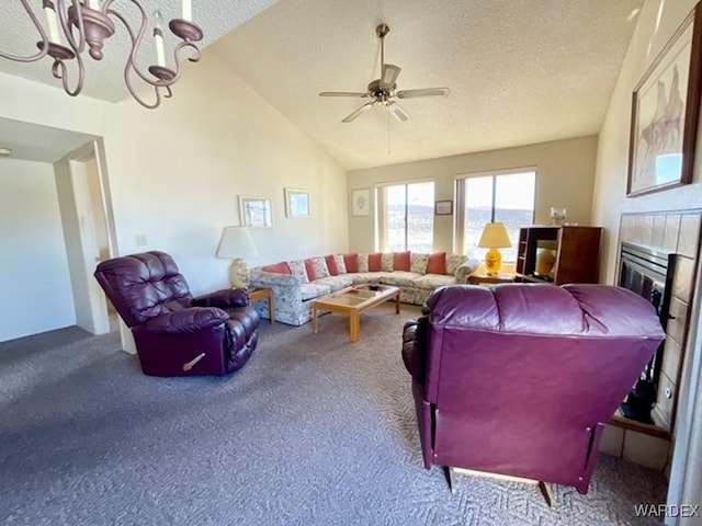 living room featuring lofted ceiling, a textured ceiling, carpet floors, a fireplace, and ceiling fan with notable chandelier