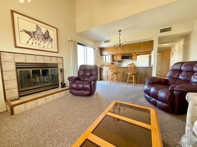 living area featuring a textured ceiling, a chandelier, carpet floors, visible vents, and a tiled fireplace