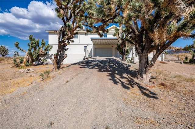 view of front of house with gravel driveway, an attached garage, and stucco siding