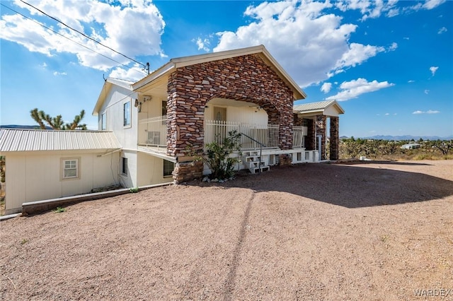 view of side of property featuring stone siding, dirt driveway, and metal roof