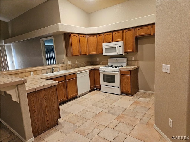 kitchen featuring white appliances, tile counters, brown cabinets, and a sink