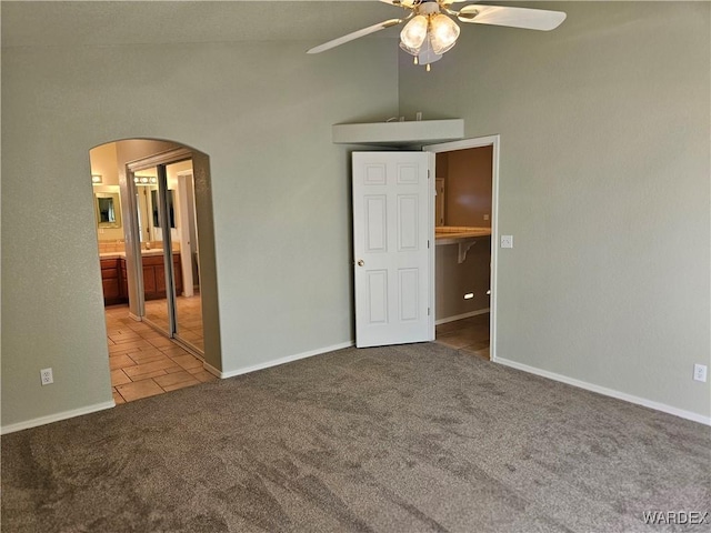 unfurnished bedroom with baseboards, arched walkways, connected bathroom, light colored carpet, and vaulted ceiling