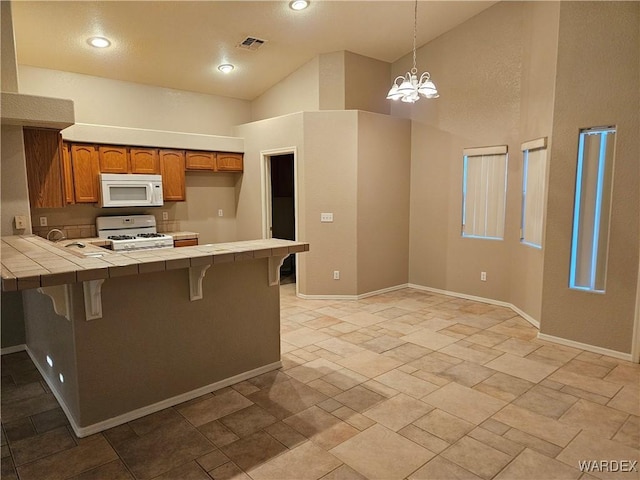 kitchen with tile countertops, a peninsula, white appliances, a breakfast bar, and brown cabinetry