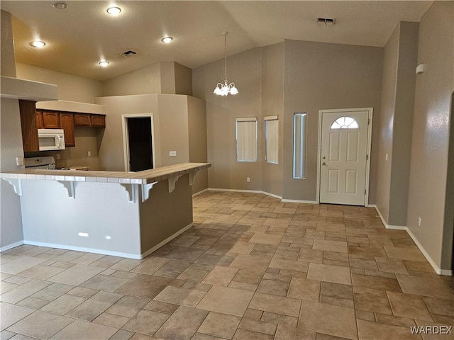 kitchen with visible vents, range, white microwave, a kitchen breakfast bar, and a peninsula