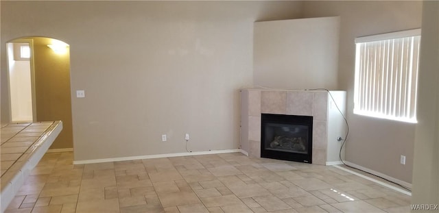 unfurnished living room with arched walkways, a fireplace, and baseboards