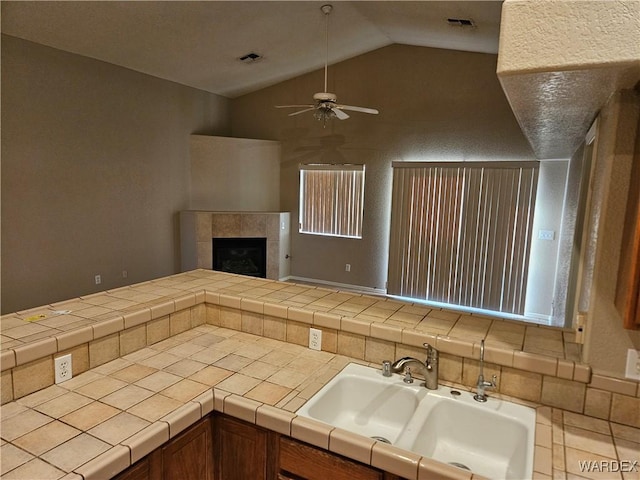 kitchen with a sink, visible vents, tile counters, brown cabinetry, and a tiled fireplace