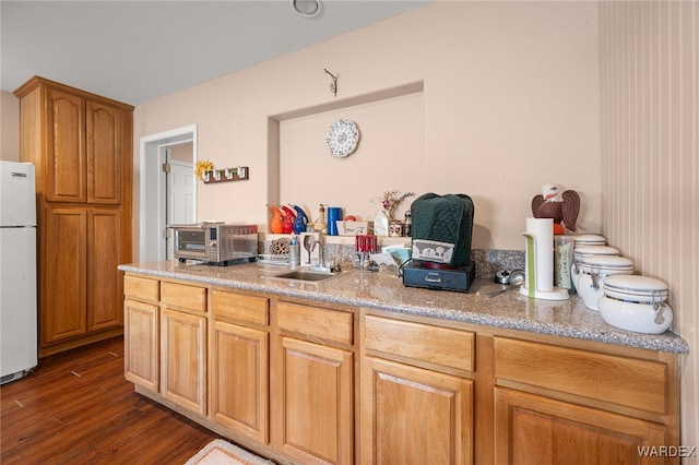 kitchen featuring a toaster, a sink, freestanding refrigerator, light stone countertops, and dark wood finished floors