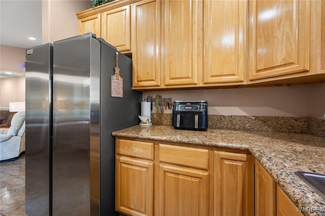 kitchen featuring light stone counters, freestanding refrigerator, light brown cabinets, and dark tile patterned floors