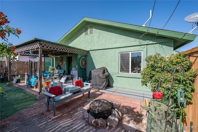 rear view of house with a fire pit, a patio, fence, and stucco siding