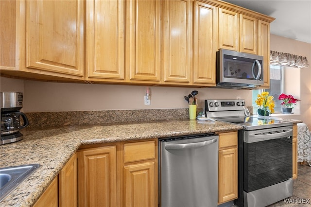 kitchen featuring light tile patterned floors, light stone counters, stainless steel appliances, and a sink