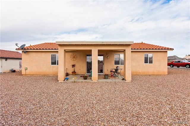 rear view of house with a tiled roof, a patio area, and stucco siding