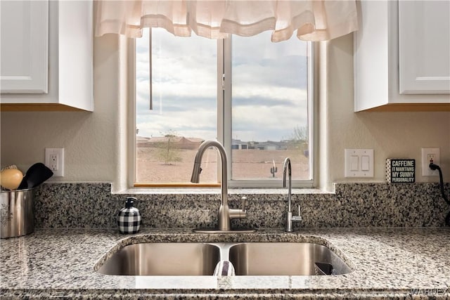 kitchen with light stone counters, white cabinetry, and a sink