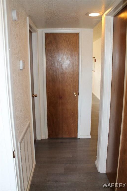 hallway with baseboards, visible vents, a textured ceiling, and wood finished floors