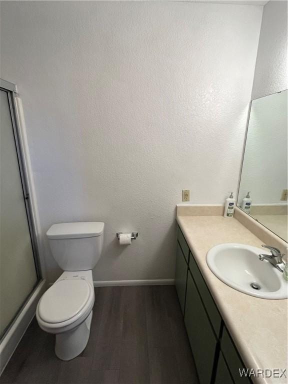 bathroom featuring toilet, a stall shower, vanity, wood finished floors, and baseboards