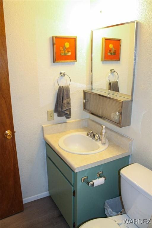 half bath featuring toilet, baseboards, wood finished floors, and vanity