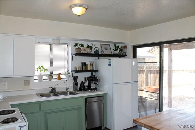 kitchen with open shelves, light countertops, a sink, white appliances, and green cabinetry