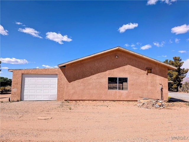 view of side of home with dirt driveway, an attached garage, and stucco siding