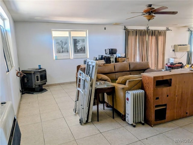 living area featuring radiator, ceiling fan, light tile patterned floors, and a wood stove