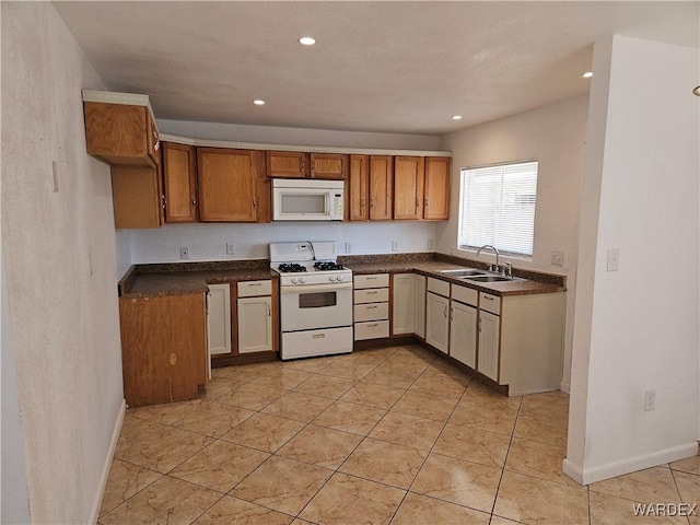 kitchen with recessed lighting, white appliances, a sink, brown cabinetry, and dark countertops