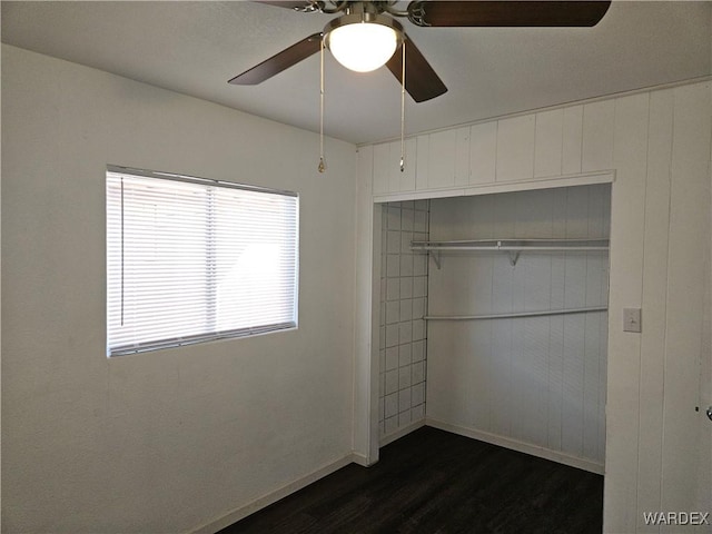 unfurnished bedroom featuring dark wood-style flooring, a closet, a ceiling fan, and baseboards