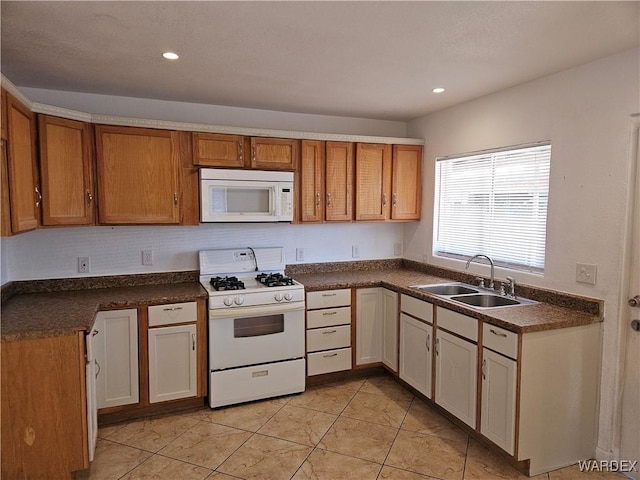 kitchen with white appliances, dark countertops, a sink, and recessed lighting